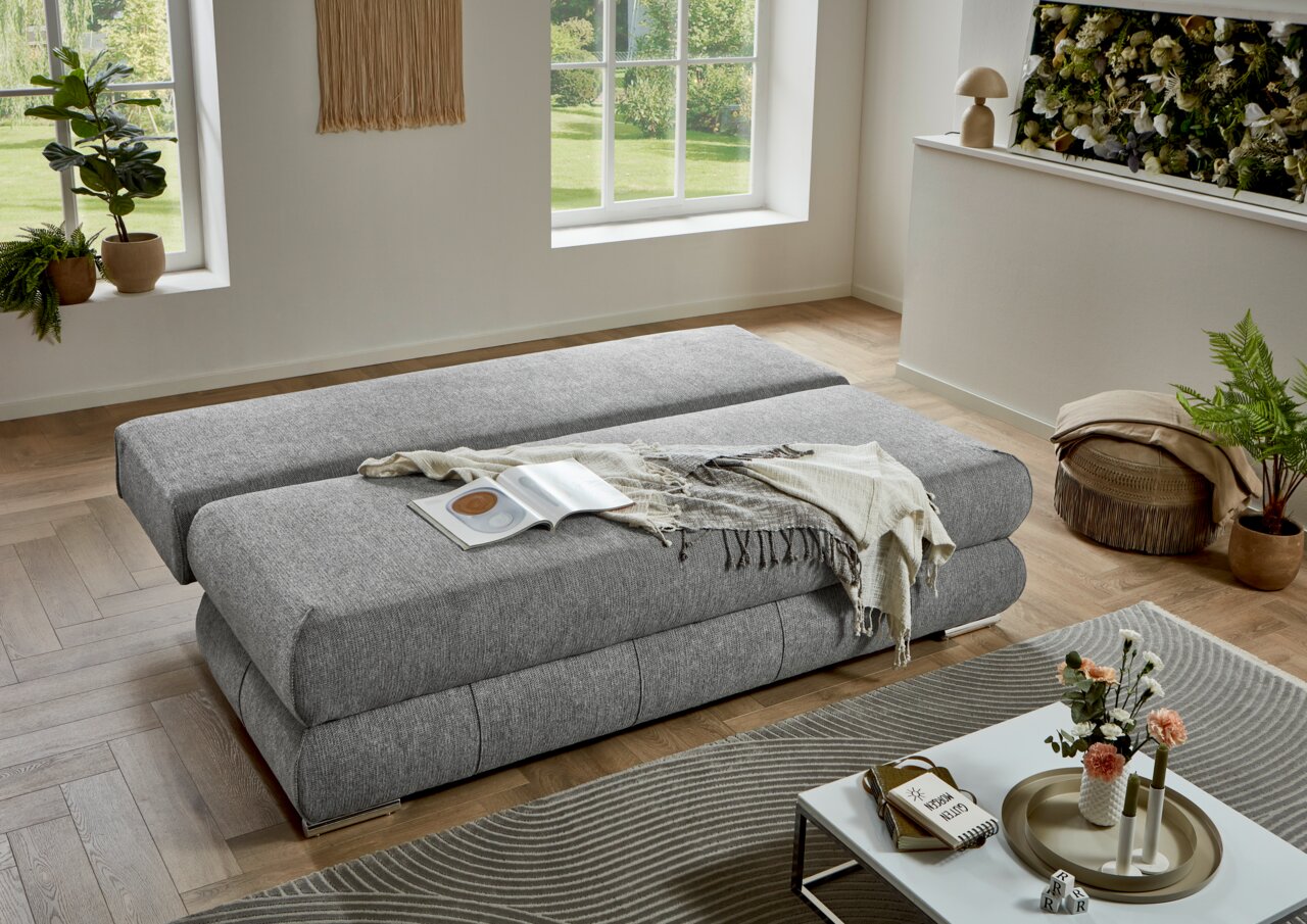 Graues Funktionssofa in einem modernen Wohnzimmer, von oben betrachtet, mit einem Buch und einer Decke darauf.