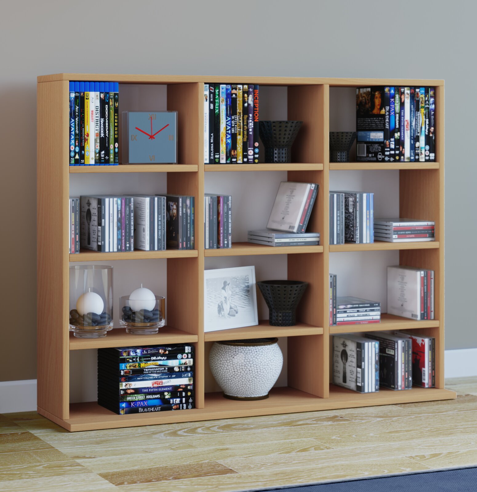 Helles Holzregal mit mehreren Fächern, gefüllt mit DVDs/Büchern und Deko (Uhr, Kerzen im Glas, Vasen), aufgenommen in frontaler Perspektive leicht von links.