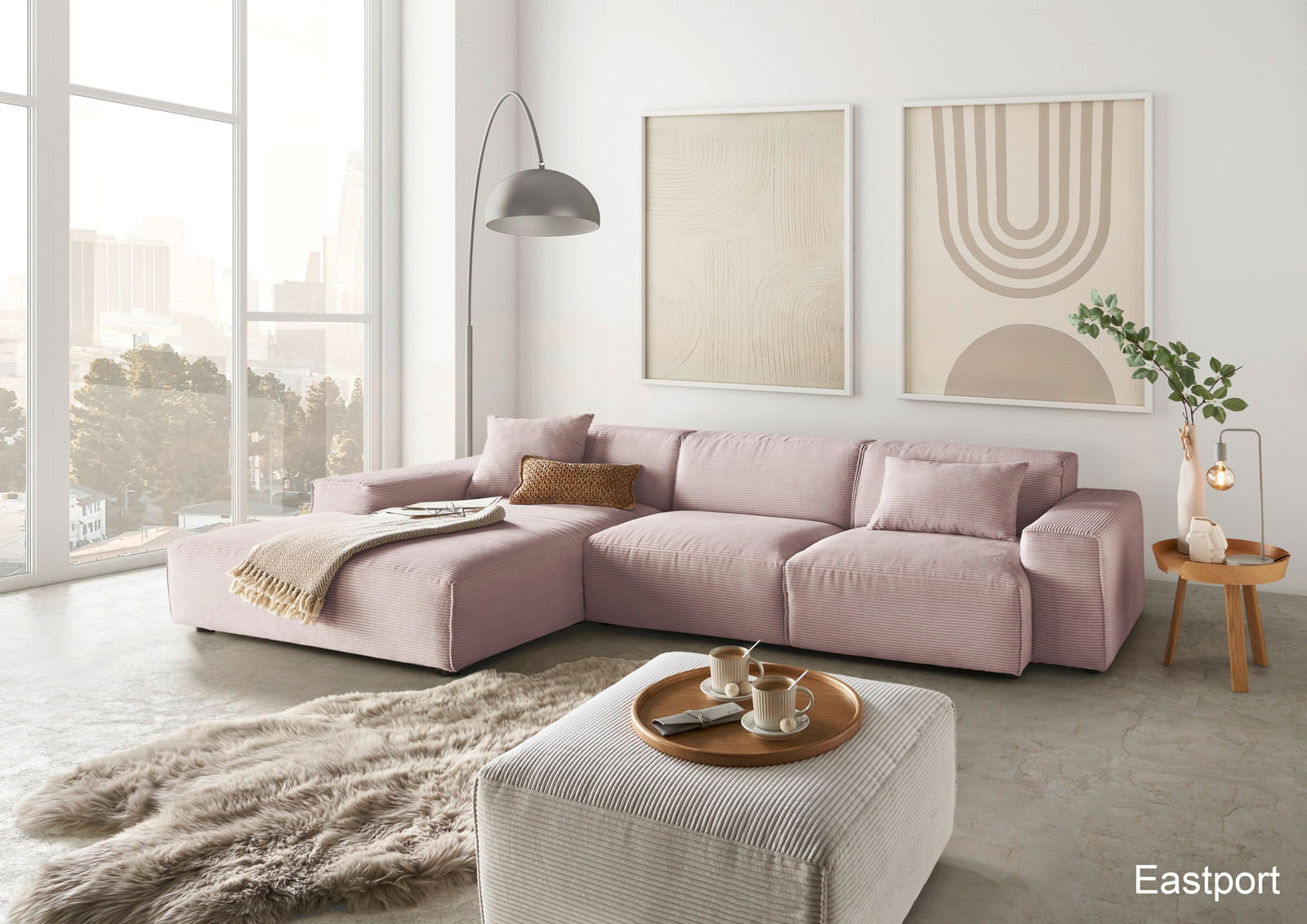 Lounge Handmade Hoekbank LH-EDINA Moderne, große Ecksofa in Rosa mit gemütlichen Kissen, abgebildet in einem hellen Wohnzimmer mit großen Fenstern und stilvollen Wandbildern, aus der Perspektive von vorne links.