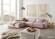 Moderne, große Ecksofa in Rosa mit gemütlichen Kissen, abgebildet in einem hellen Wohnzimmer mit großen Fenstern und stilvollen Wandbildern, aus der Perspektive von vorne links.