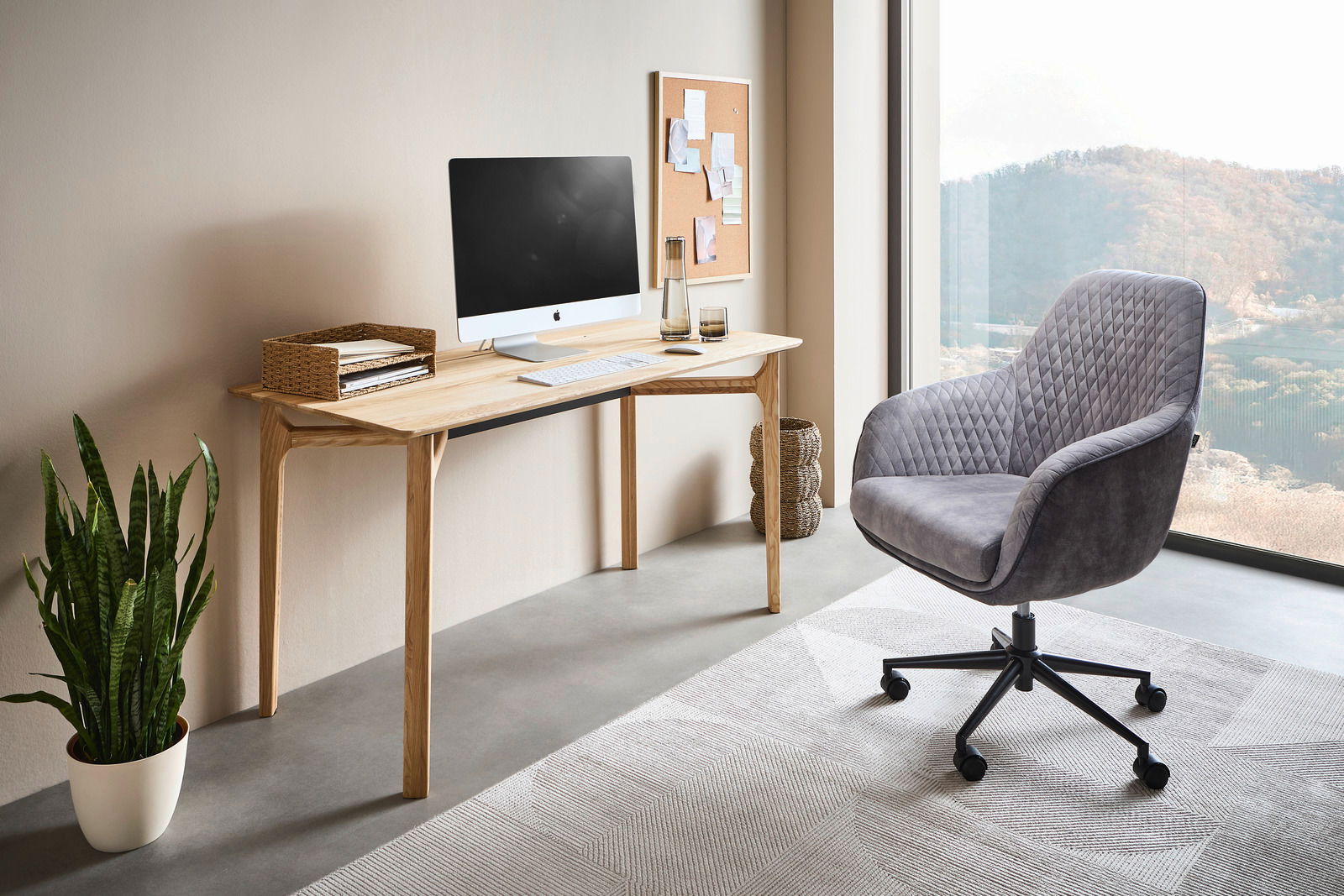 Moderner Schreibtisch aus Holz mit Computer, Pflanzen und Bürostuhl in einem hellen Raum mit Blick auf die Landschaft, seitliche Perspektive.