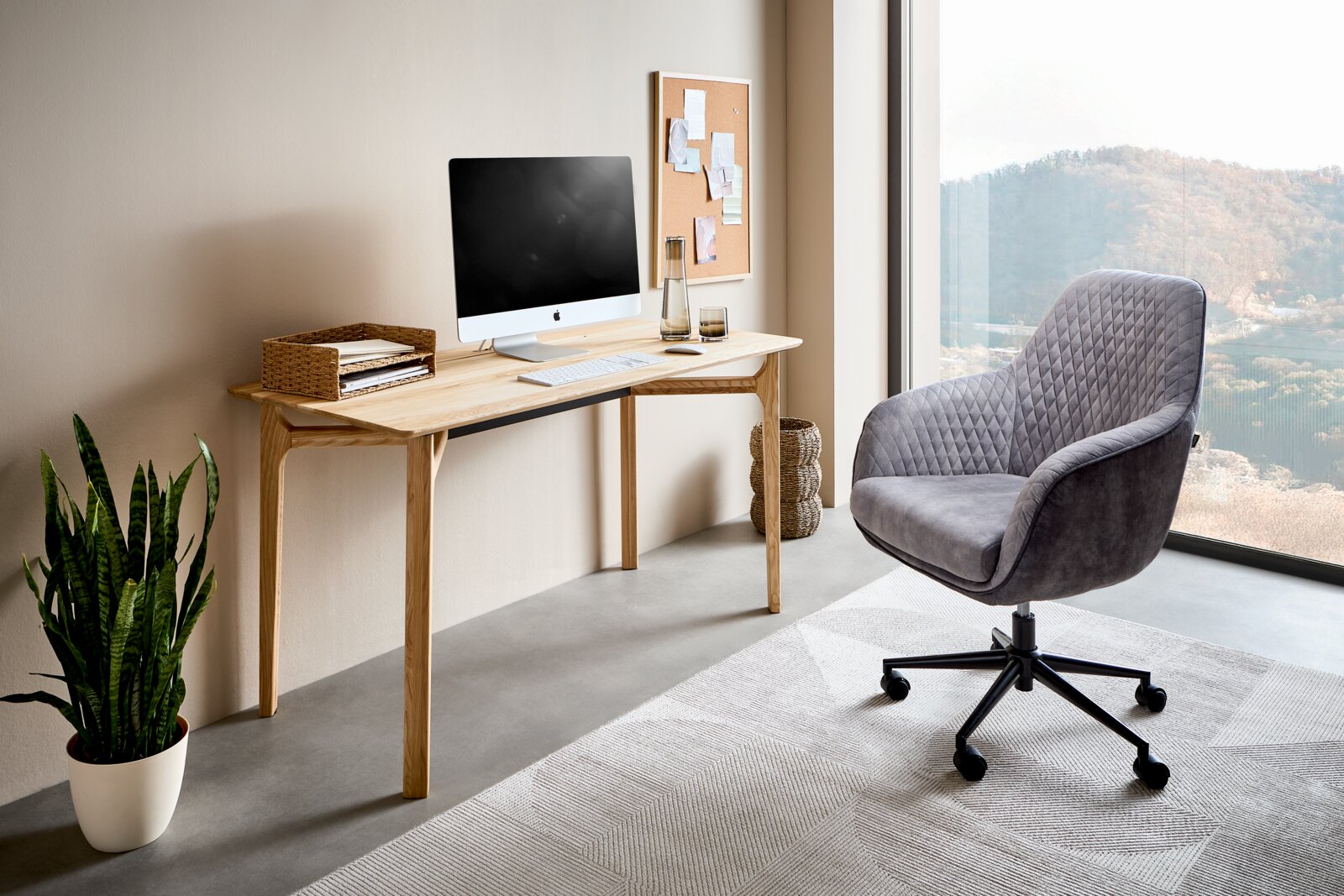 Modern houten bureau met computer, planten en bureaustoel in een lichte ruimte met uitzicht op het landschap, zijaanzicht.