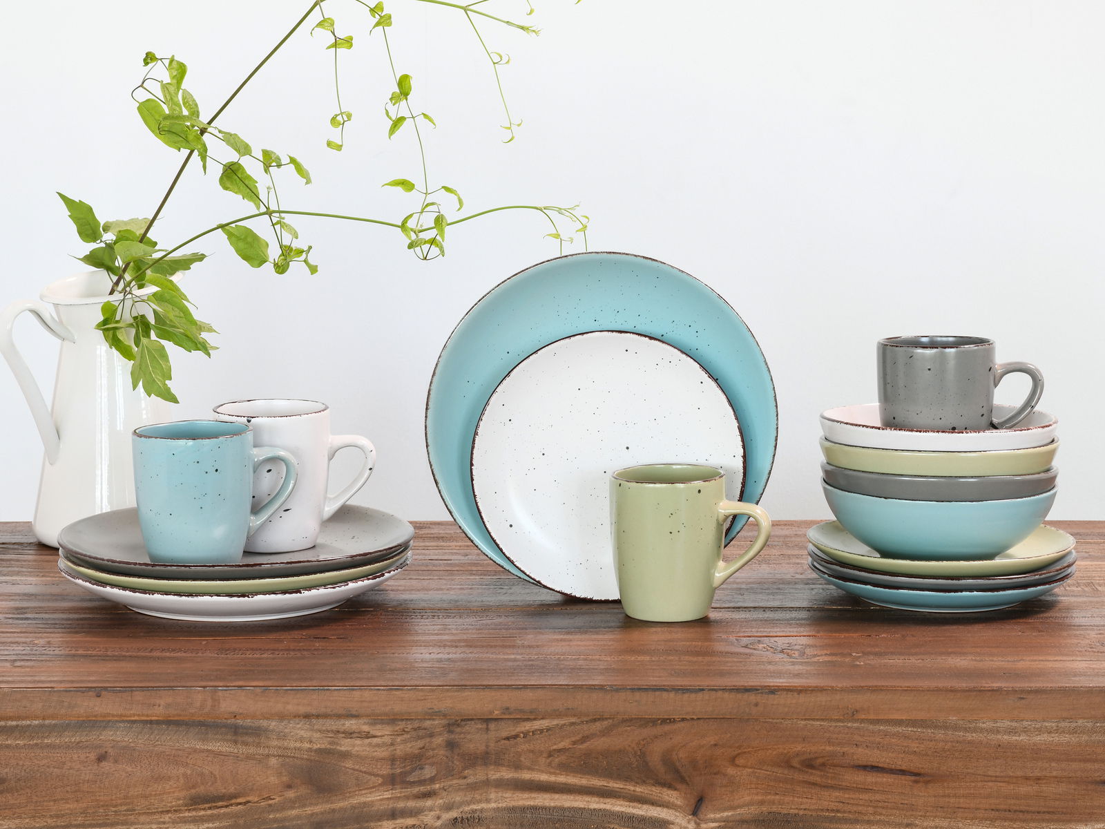 Kombiservice 16-tlg. Fashion in verschiedenen Pastellfarben, bestehend aus Tellern und Tassen, auf einem Holztisch arrangiert. Seitliche Perspektive.