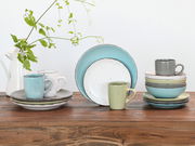 Kombiservice 16-tlg. Fashion in verschiedenen Pastellfarben, bestehend aus Tellern und Tassen, auf einem Holztisch arrangiert. Seitliche Perspektive.