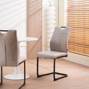 Beiger Polster-Esszimmerstuhl in Velours-/Wildlederoptik mit schwarzem Freischwinger-Metallgestell, im Wohn-/Essbereich neben rundem weißem Tisch; Perspektive: frontale leicht seitliche Ansicht auf Sitz und Rückenlehne