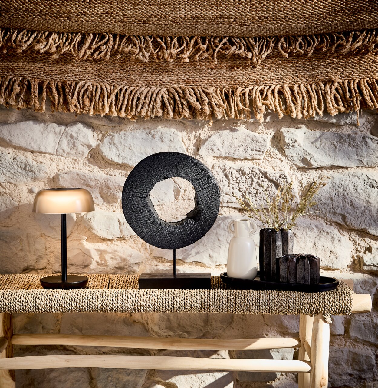 Ambia Garden Solar-Akku-Tischleuchte OKLAHOMA Solarleuchte Ambia Garden auf einem Tisch, seitliche Perspektive, umgeben von Dekorationen vor einer Steinwand.