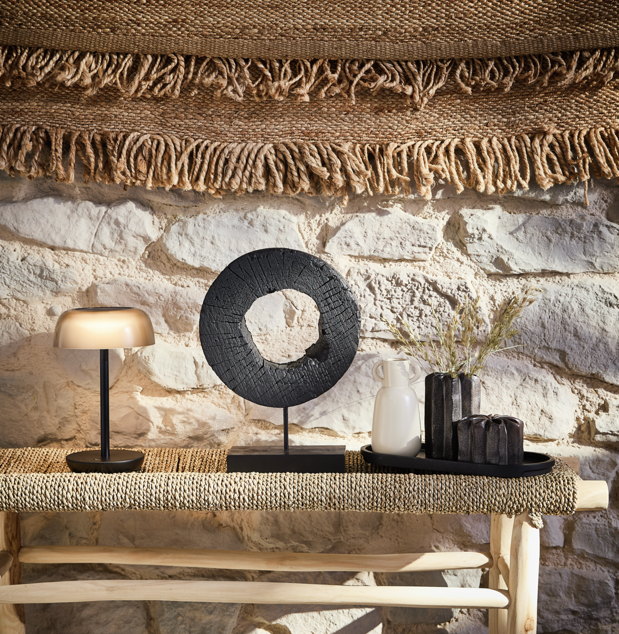 Solarleuchte Ambia Garden auf einem Tisch, seitliche Perspektive, umgeben von Dekorationen vor einer Steinwand.