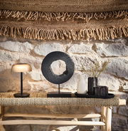 Solarleuchte Ambia Garden auf einem Tisch, seitliche Perspektive, umgeben von Dekorationen vor einer Steinwand.