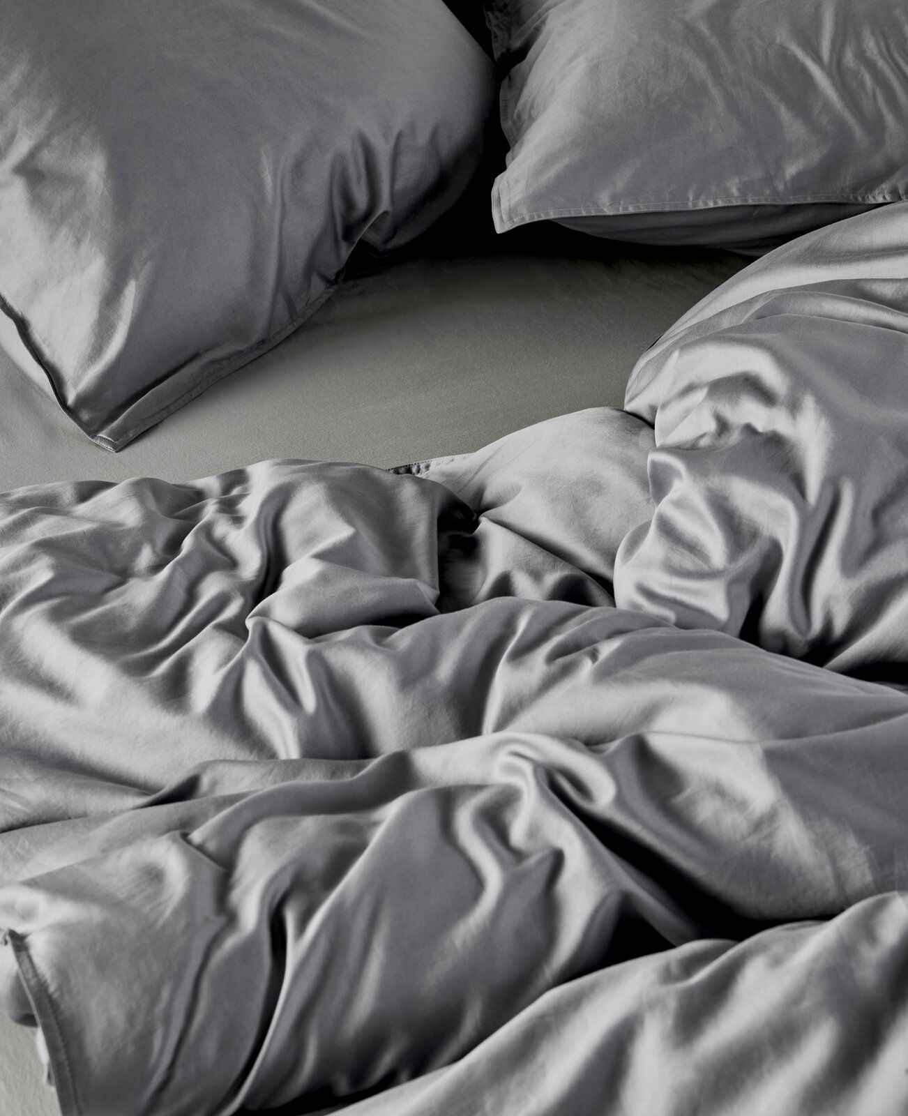 Graue Bettwäsche aus Baumwolle in Nahaufnahme, zeigt Kissen und Decke in einer gemütlichen, ungemachten Anordnung.