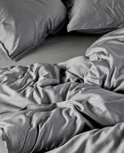 Graue Bettwäsche aus Baumwolle in Nahaufnahme, zeigt Kissen und Decke in einer gemütlichen, ungemachten Anordnung.