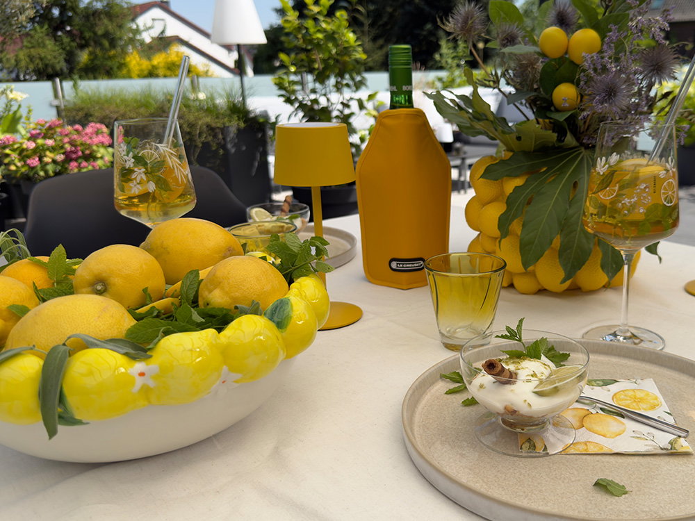 Sommerliche Tischdekoration mit Zitronen, Desserts und Getränken auf der Terrasse.