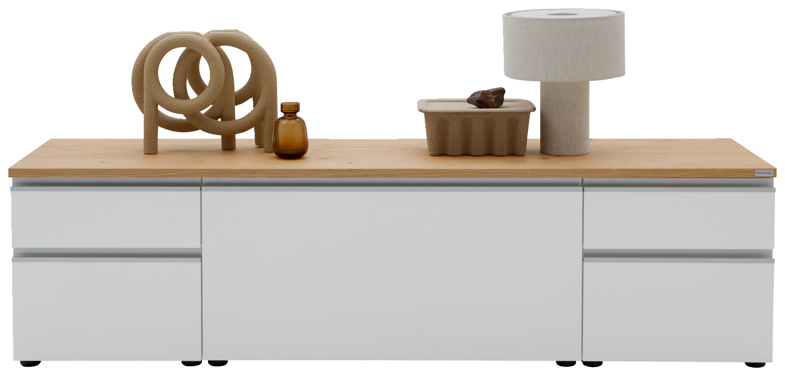 Modernes Lowboard/Sideboard in Hellgrau mit Eichenholzplatte, frontale Ansicht; oben Deko mit Skulptur, brauner Glasvase, Schale und Tischlampe vor weißem Hintergrund.