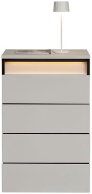 Hochkommode mit vier Schubladen, moderne graue Oberfläche, beleuchtetes Fach oben, Ansicht von vorne, dekoriert mit einer Tischlampe und einem Buch.