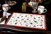 Kerstachtige gobelin-placemat met speelgoedmotieven en een rode rand, van bovenaf gefotografeerd op een gedekte tafel.