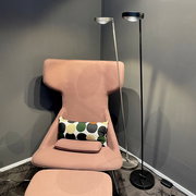 Zwei moderne LED-Stehleuchten, eine silberne und eine schwarze, stehen neben einem rosa Sessel mit einem bunten Kissen. Perspektive: seitlich.