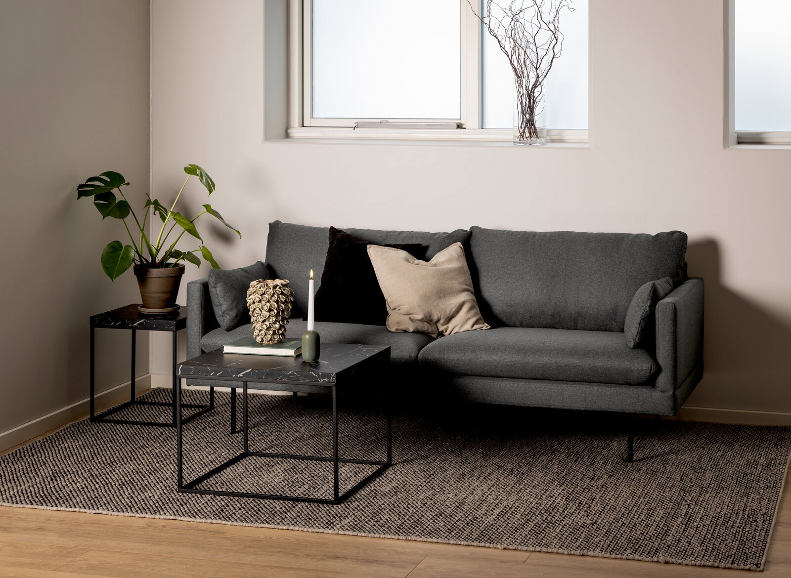 Moderner Couchtisch mit schwarzer Marmoroptik und Metallgestell, frontal vor einem grauen Sofa in einem stilvoll eingerichteten Wohnzimmer.