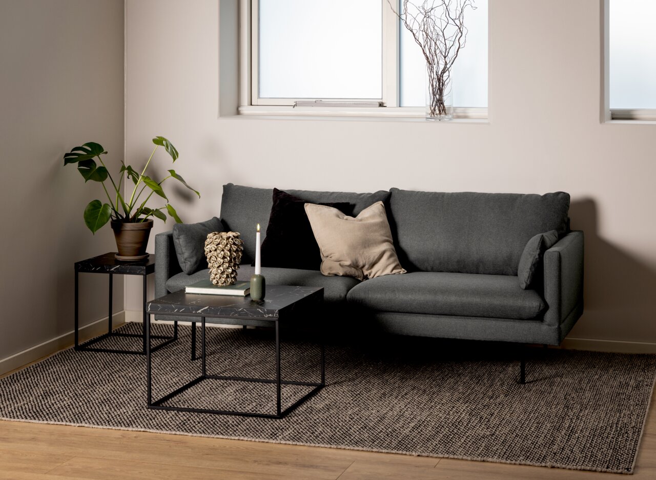 Moderner Couchtisch mit schwarzer Marmoroptik und Metallgestell, frontal vor einem grauen Sofa in einem stilvoll eingerichteten Wohnzimmer.