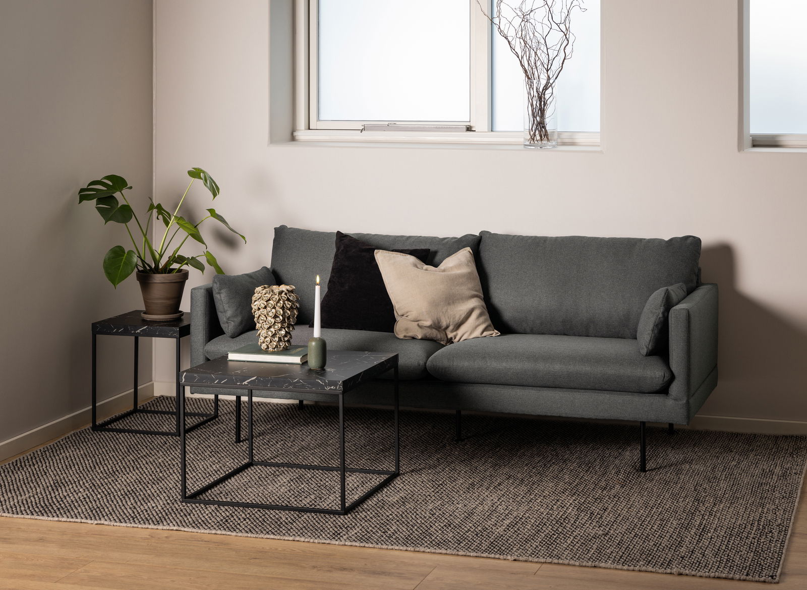 Moderner Couchtisch mit schwarzer Marmoroptik und Metallgestell, frontal vor einem grauen Sofa in einem stilvoll eingerichteten Wohnzimmer.