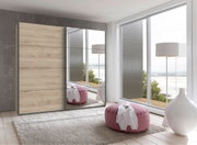 Moderner Schwebetürenschrank mit zwei Türen, eine in Holzoptik und die andere verspiegelt, in einem hellen Raum mit großen Fenstern und Blick auf das Wasser. Perspektive von vorne.