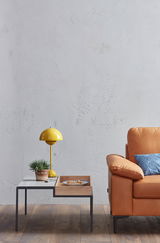 Teilansicht eines modernen Sofas in Lederoptik mit einem blauen Kissen, daneben ein Beistelltisch mit gelber Lampe und Pflanze, aus seitlicher Perspektive.