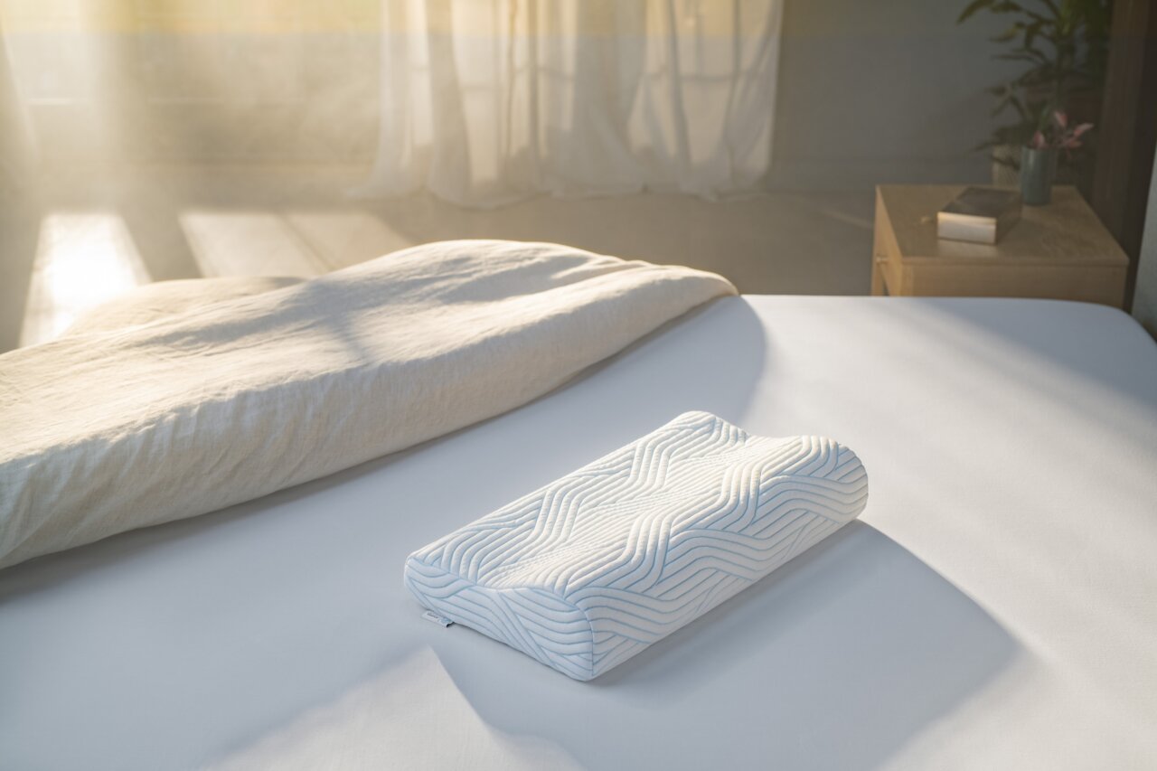 Tempur Slaapkussen SHAPE Schlafkissen 61 x 31 cm auf einem Bett, seitliche Perspektive, mit Sonnenlicht im Hintergrund