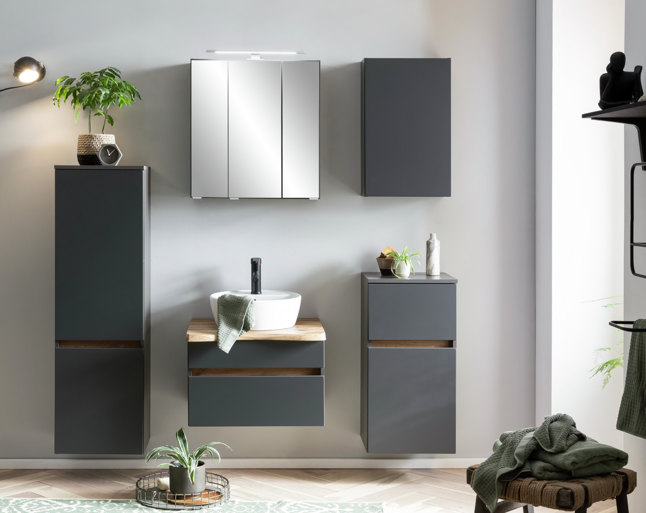 Moderne Badezimmermöbel in dunklem Grau mit Holzakzenten, bestehend aus einem Unterschrank mit Waschbecken, einem hohen Schrank, einem Hängeschrank und einem Spiegelschrank, frontal betrachtet.