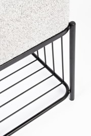 Close-up van een kruk met een zwart metalen frame en lichtgrijze bekleding, gezien vanaf de zijkant.