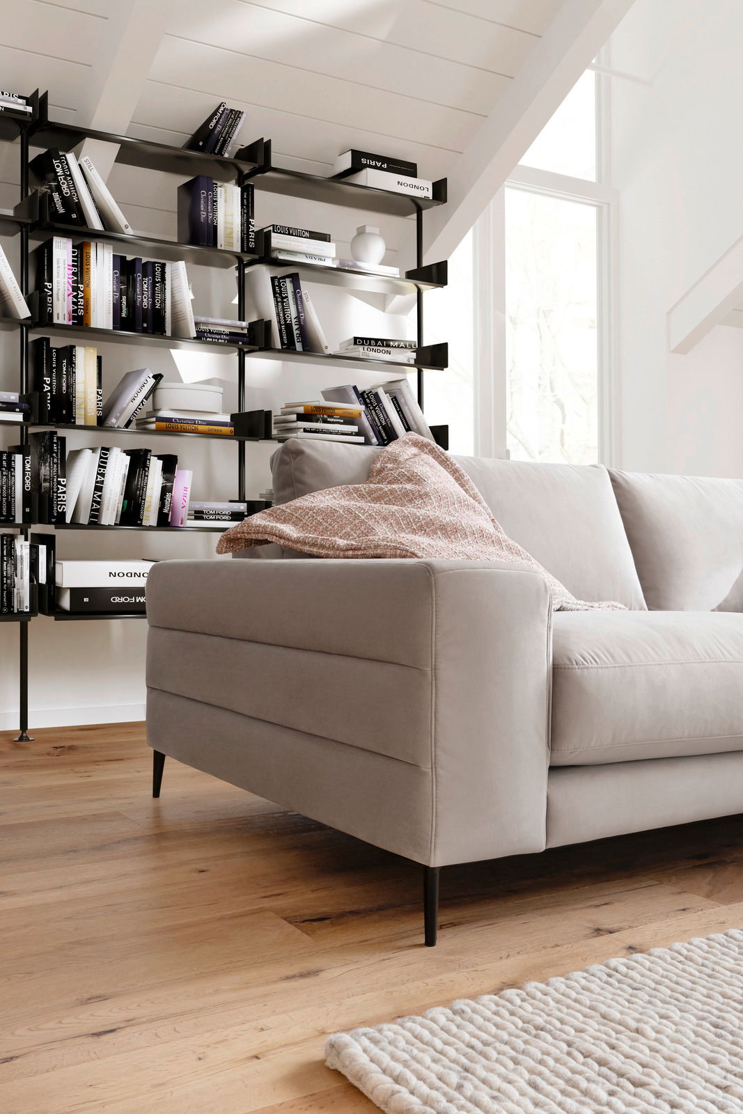 Beige Longchairkombination in einem modernen Wohnzimmer, seitliche Perspektive mit Bücherregal im Hintergrund.