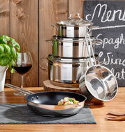 Perspektive: Frontalansicht auf ein 5-teiliges Topfset aus Edelstahl, bestehend aus gestapelten Töpfen mit Deckeln und einer Pfanne im Vordergrund, dekoriert mit frischen Kräutern und einem Glas Rotwein.