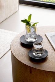 Zwei Espressountertassen aus der Manufacture-Serie auf einem Holztisch, mit Gläsern gefüllt mit Wasser und Minze, aus einer seitlichen Perspektive fotografiert.