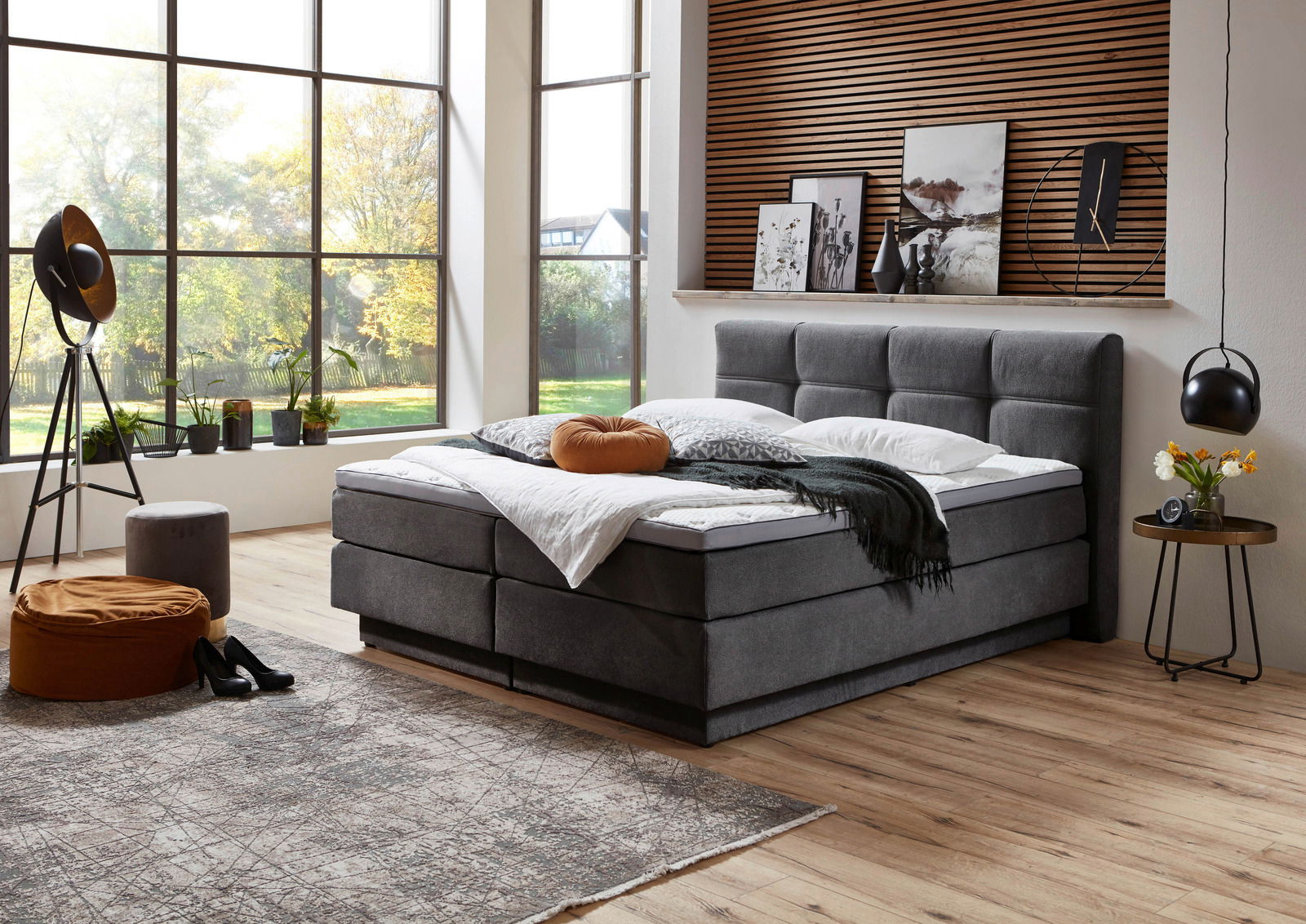Modernes Boxspringbett in einem stilvollen Schlafzimmer mit großen Fenstern, seitliche Perspektive.