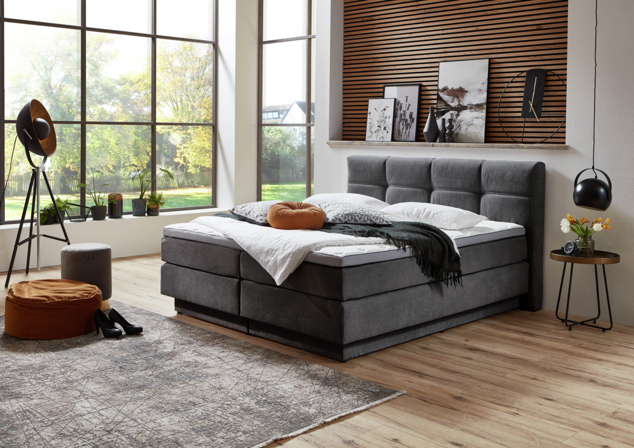Modernes Boxspringbett in einem stilvollen Schlafzimmer mit großen Fenstern, seitliche Perspektive.