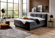 Modernes Boxspringbett in einem stilvollen Schlafzimmer mit großen Fenstern, seitliche Perspektive.
