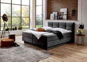 Modernes Boxspringbett in einem stilvollen Schlafzimmer mit großen Fenstern, seitliche Perspektive.