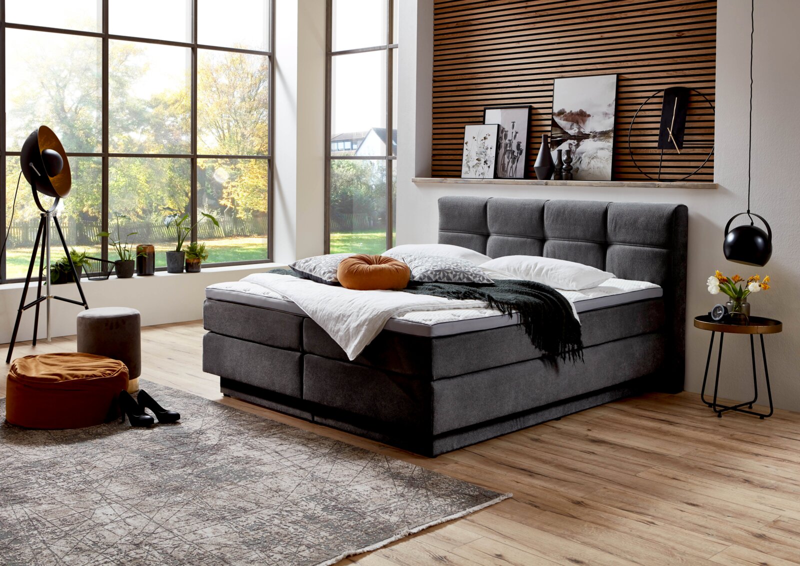Modernes Boxspringbett in einem stilvollen Schlafzimmer mit großen Fenstern, seitliche Perspektive.