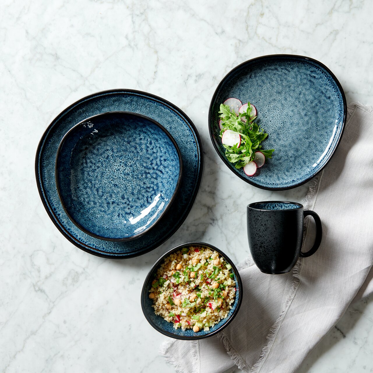 Kombiservice 10-tlg. in Blau mit gesprenkeltem Design, bestehend aus Tellern, Schalen und einer Tasse, von oben fotografiert auf einem Marmortisch.