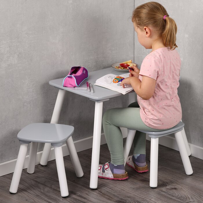 Kindersitzgruppe mit grauem Tisch und zwei passenden Hockern, weiß-graues Design, ein Mädchen sitzt seitlich/rechts im Profil am Tisch und malt; Perspektive: seitliche Ansicht auf Tisch und Hocker in einer Zimmerecke