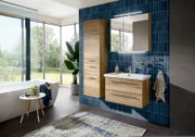 Modernes Badezimmer mit hängendem Waschtisch und Hochschrank in Holzoptik, weißem Waschbecken, Spiegelschrank mit LED-Leuchte vor blauen Fliesen; Perspektive: frontale, leicht seitliche Ansicht auf die Badmöbel.