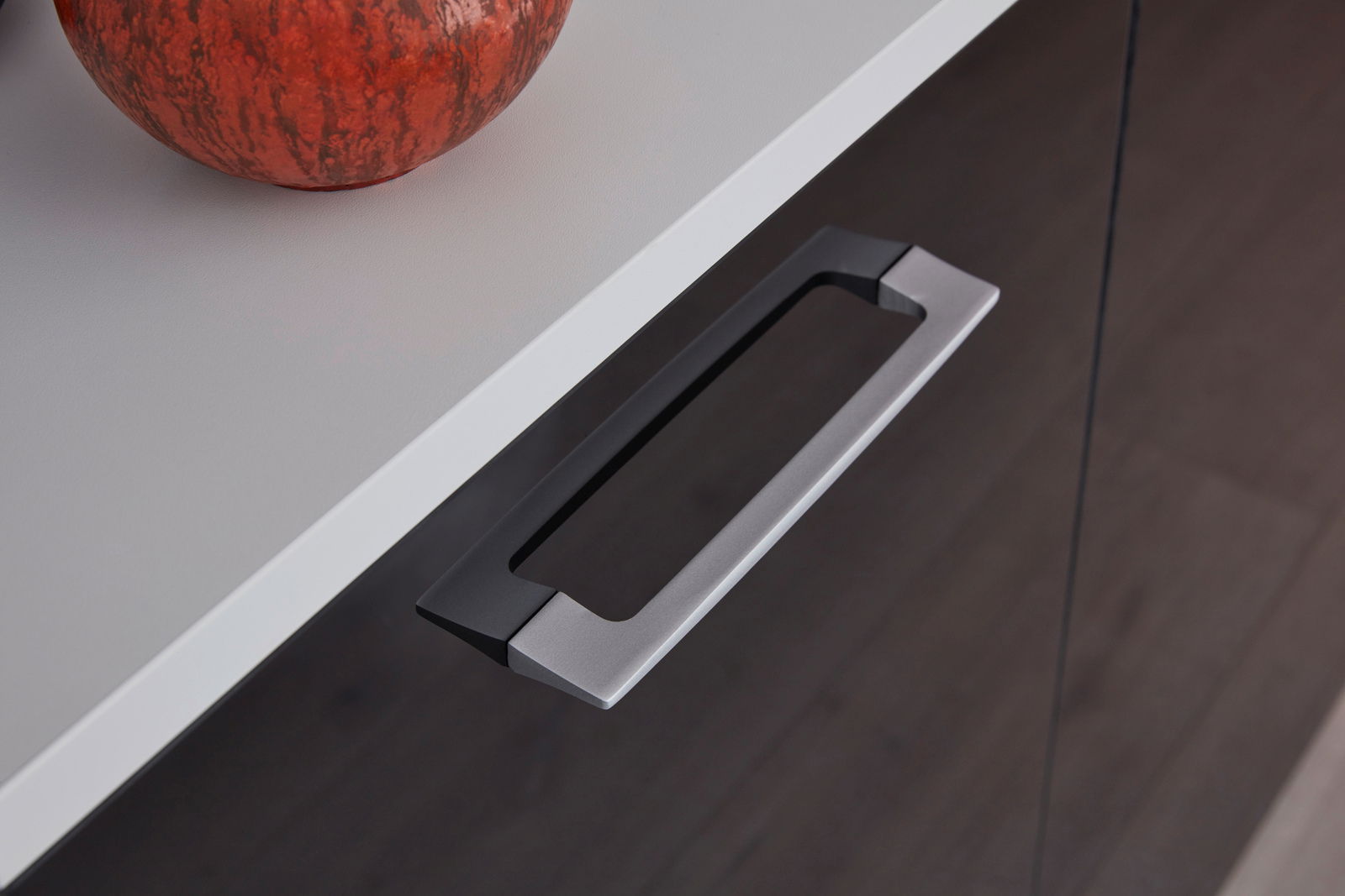 Nahaufnahme eines Sideboards mit modernem Metallgriff und dekorativem Kürbis auf der Oberfläche, von oben fotografiert.