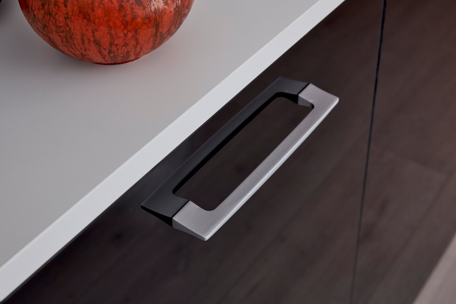 Close-up van een dressoir met een moderne metalen handgreep en een decoratieve pompoen op het blad, gefotografeerd van bovenaf.