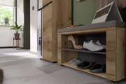 Garderobenbank aus Holz mit grauem Polster, seitliche Perspektive, mit Schuhen auf zwei Ebenen und einem Laptop auf der Sitzfläche.
