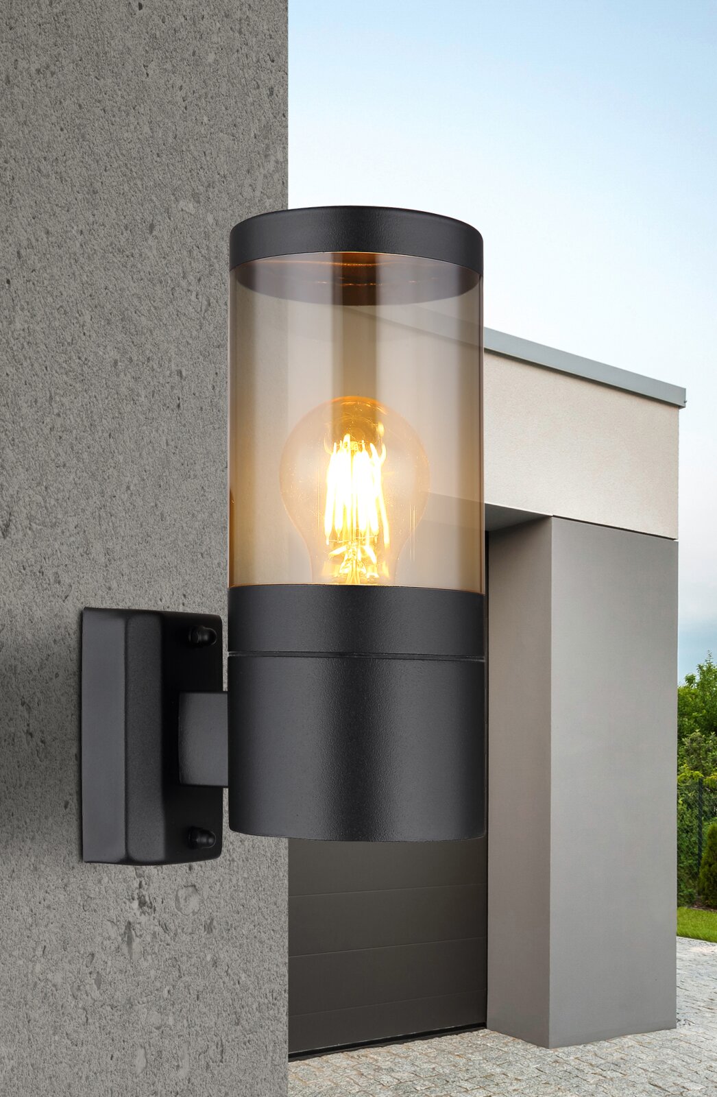 Moderne Außenleuchte mit zylindrischem Glasdesign, an einer Betonwand montiert, seitliche Perspektive.
