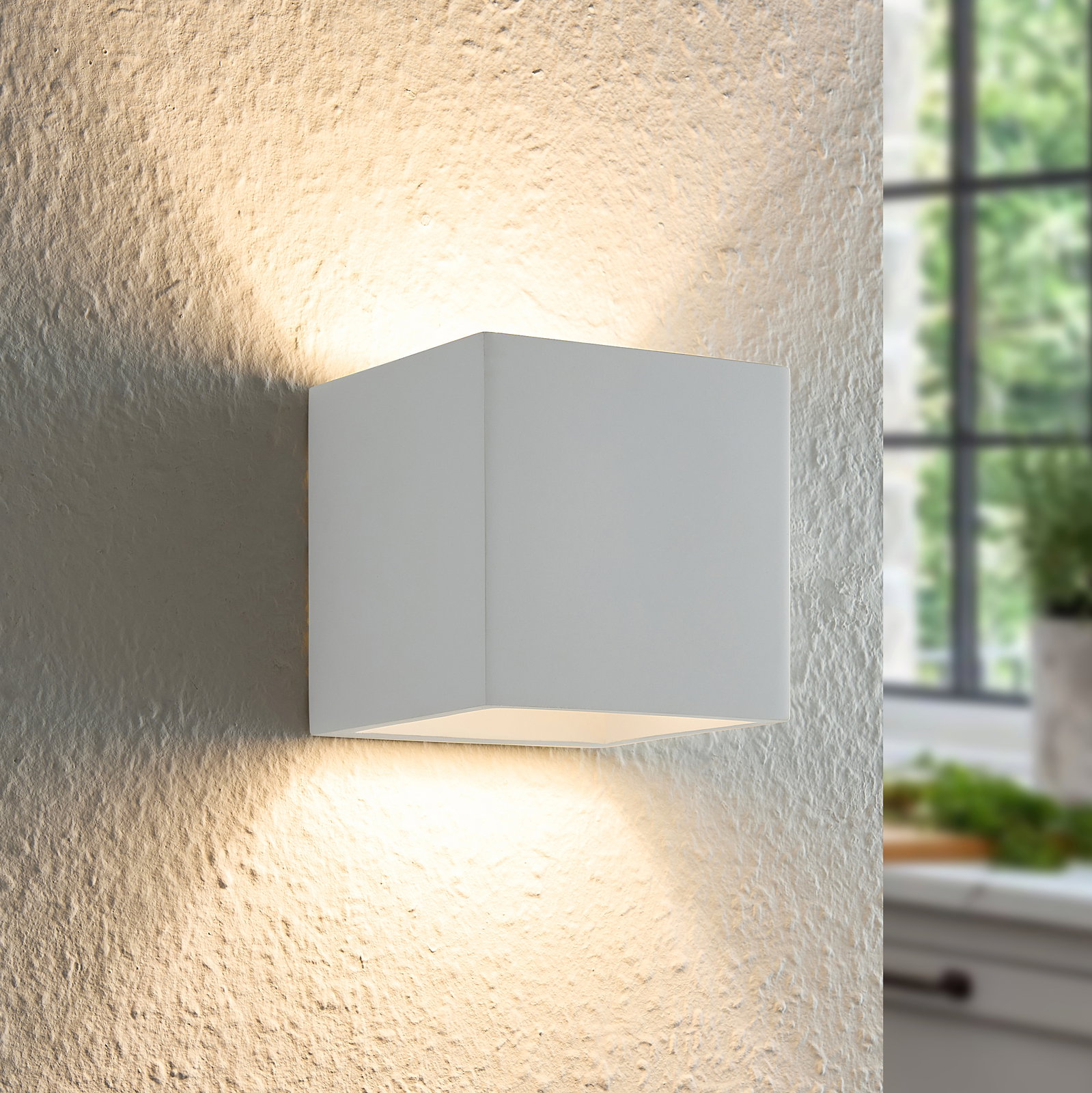 Moderne weiße Wandleuchte in Würfelform, die an einer strukturierten Wand montiert ist und warmes Licht nach oben und unten abstrahlt, seitliche Perspektive.
