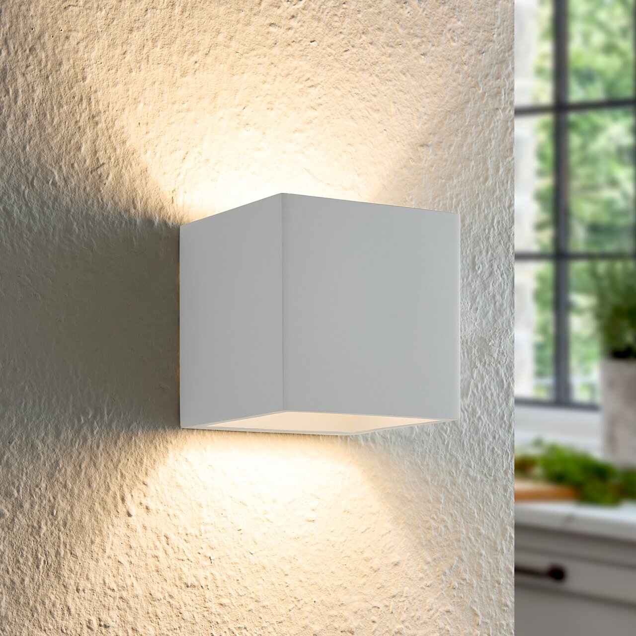 Moderne weiße Wandleuchte in Würfelform, die an einer strukturierten Wand montiert ist und warmes Licht nach oben und unten abstrahlt, seitliche Perspektive.