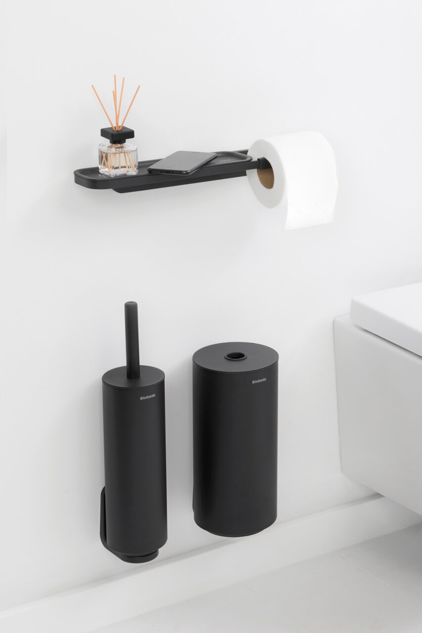 Zwarte toiletrolhouder met opbergvak, met daarop een geurverspreider en een smartphone, gezien vanaf de zijkant.