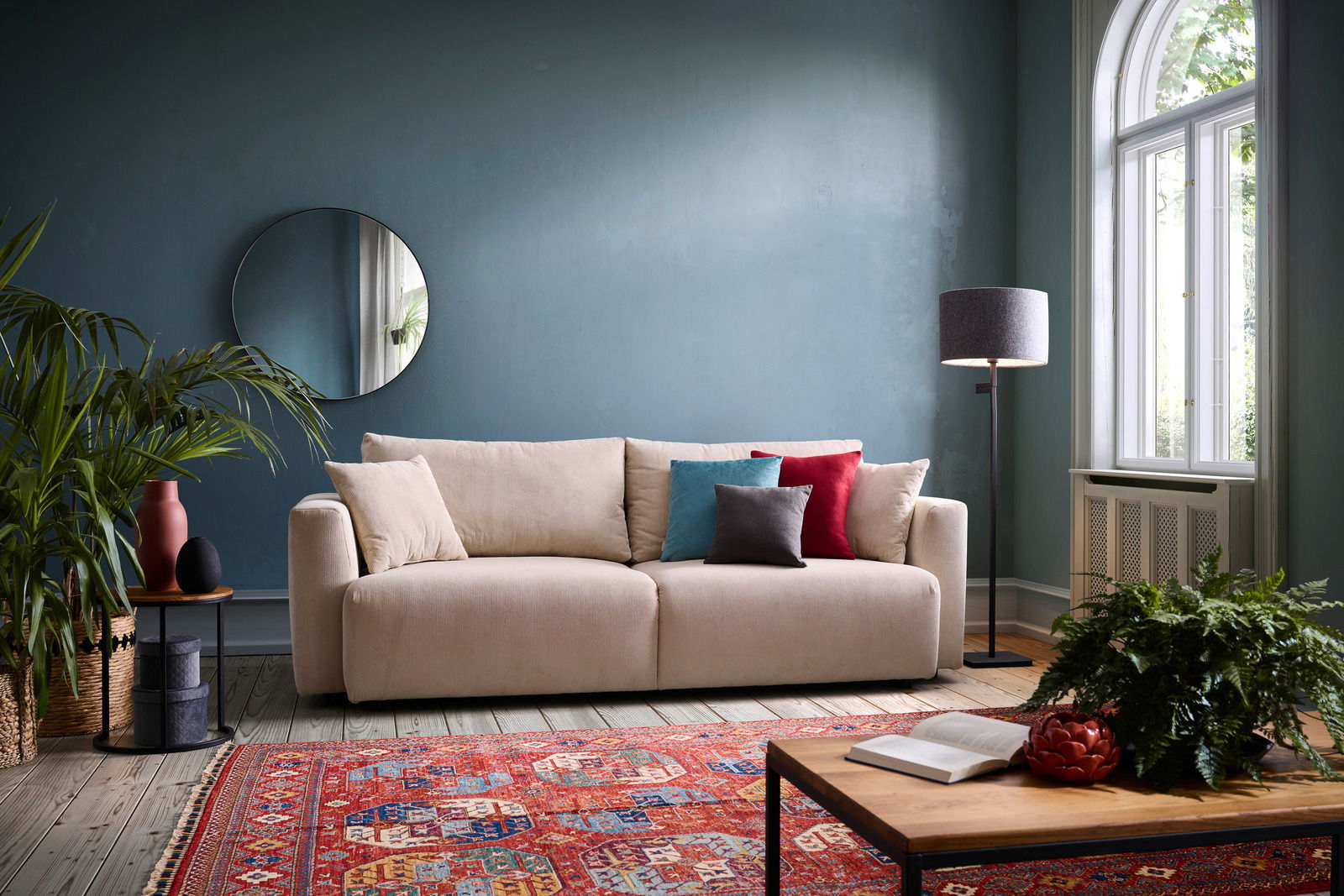 Z2 Schlafsofa PONTE Beiges Funktionssofa PONTE in einem stilvoll eingerichteten Wohnzimmer mit blauen Wänden, dekorativen Kissen und einem runden Spiegel, aus frontaler Perspektive.