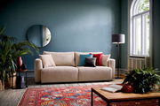 Beiges Funktionssofa PONTE in einem stilvoll eingerichteten Wohnzimmer mit blauen Wänden, dekorativen Kissen und einem runden Spiegel, aus frontaler Perspektive.