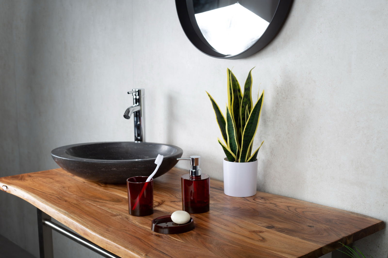 Moderner Seifenspender in transparentem Design auf einem Holzwaschtisch, neben einem Waschbecken und einer Pflanze, aus seitlicher Perspektive.