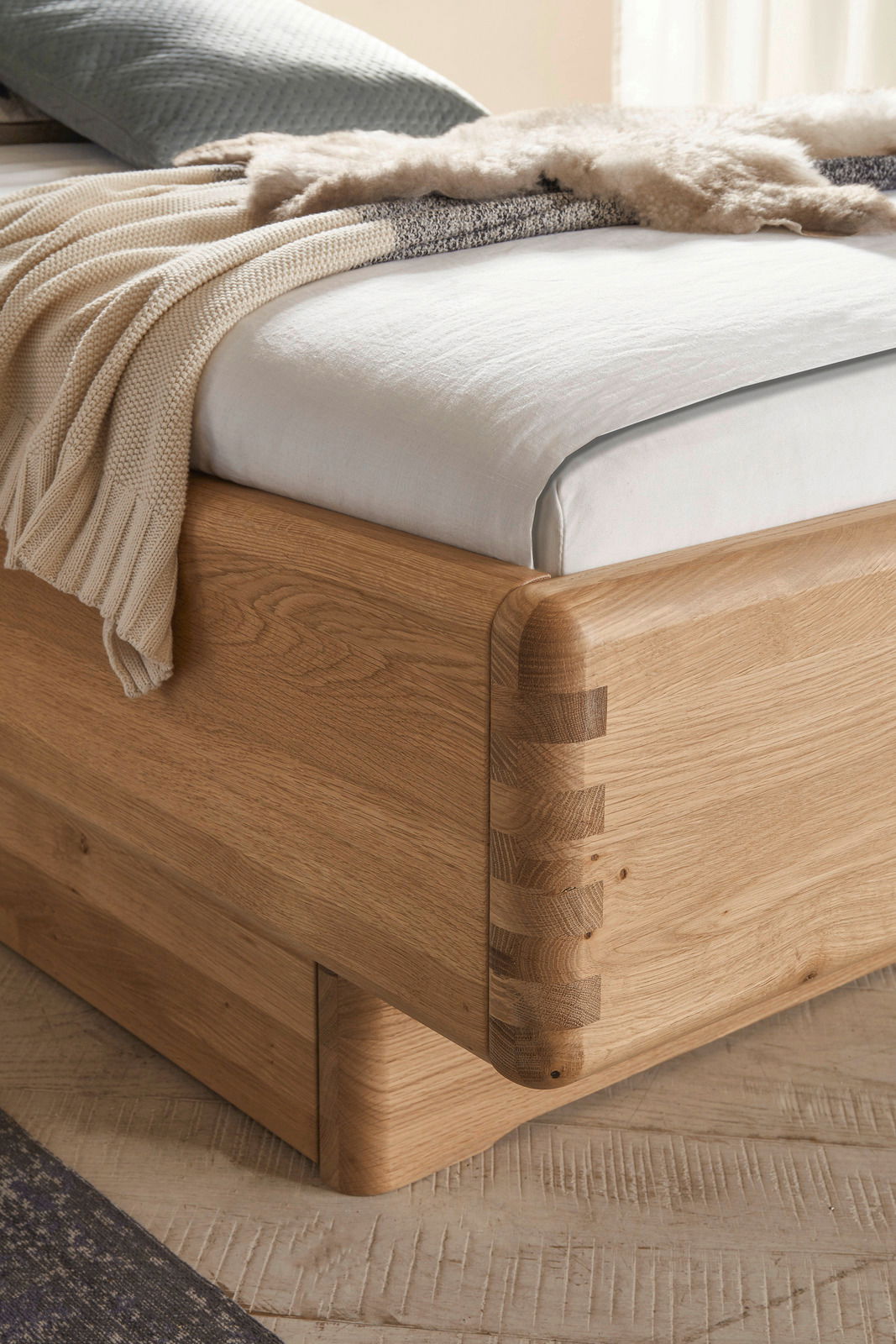 Nahaufnahme eines Bettgestells aus Holz mit sichtbaren Eckverbindungen, von der Seite betrachtet.