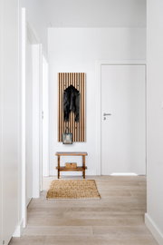 Moderne Wandgarderobe XORA GRACE in einem hellen Flur, frontal fotografiert, mit einer schwarzen Jacke und einer Tasche dekoriert.